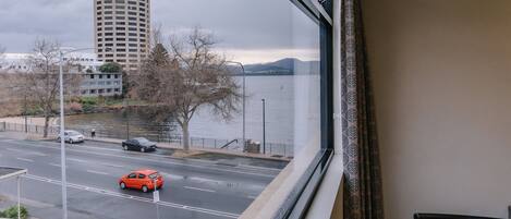 A view from a window overlooking a road with cars, a tall building, and a body of water.