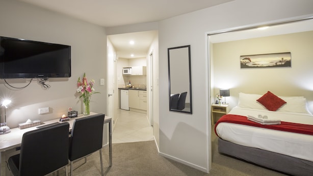 Ein Hotelzimmer mit einem Bett, einem Schreibtisch mit Stühlen, einem Fernseher, einem Bild und einer Küche im Hintergrund.