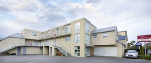 Ett flervåningsmotell med en central trappa, ett överbyggt parkeringsområde och en synlig bil på parkeringen.