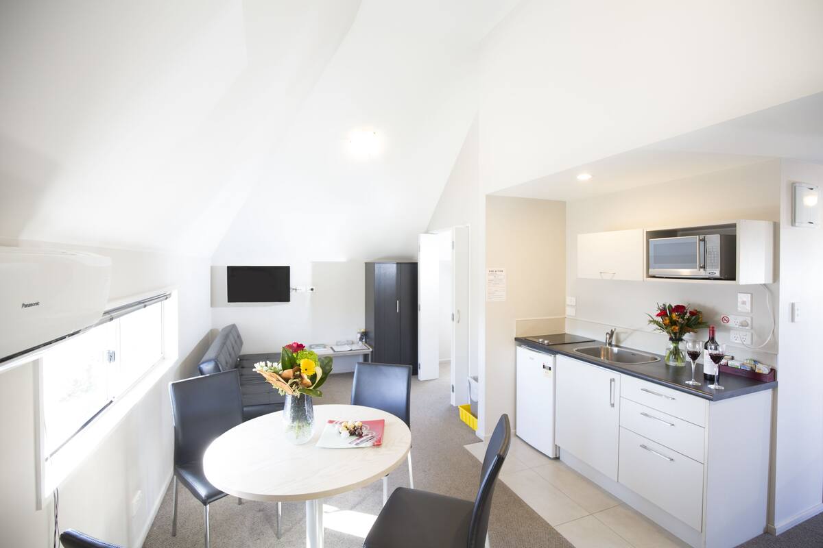 Eine moderne Küche mit weißen Schränken, einer Mikrowelle und einem Spülbecken. Ein Essbereich mit Tisch und Stühlen, sowie eine Couch im Hintergrund.