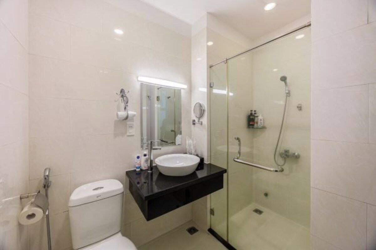 A modern bathroom with a glass-enclosed shower, a white toilet, and a black vanity with a sink and mirror.