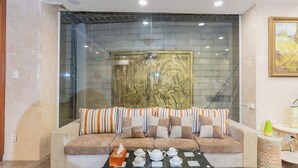 A modern lobby with a beige sofa, striped cushions, a glass partition, and a decorative wall piece.