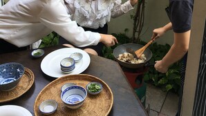 Un groupe de personnes prépare des aliments à l’extérieur, autour d’une table dressée avec des assiettes, des bols et un tapis tissé.