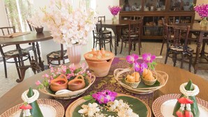Un coin repas avec une table ronde dressée avec de la vaisselle traditionnelle, un vase rempli de fleurs roses et, au fond, un buffet aux portes vitrées.