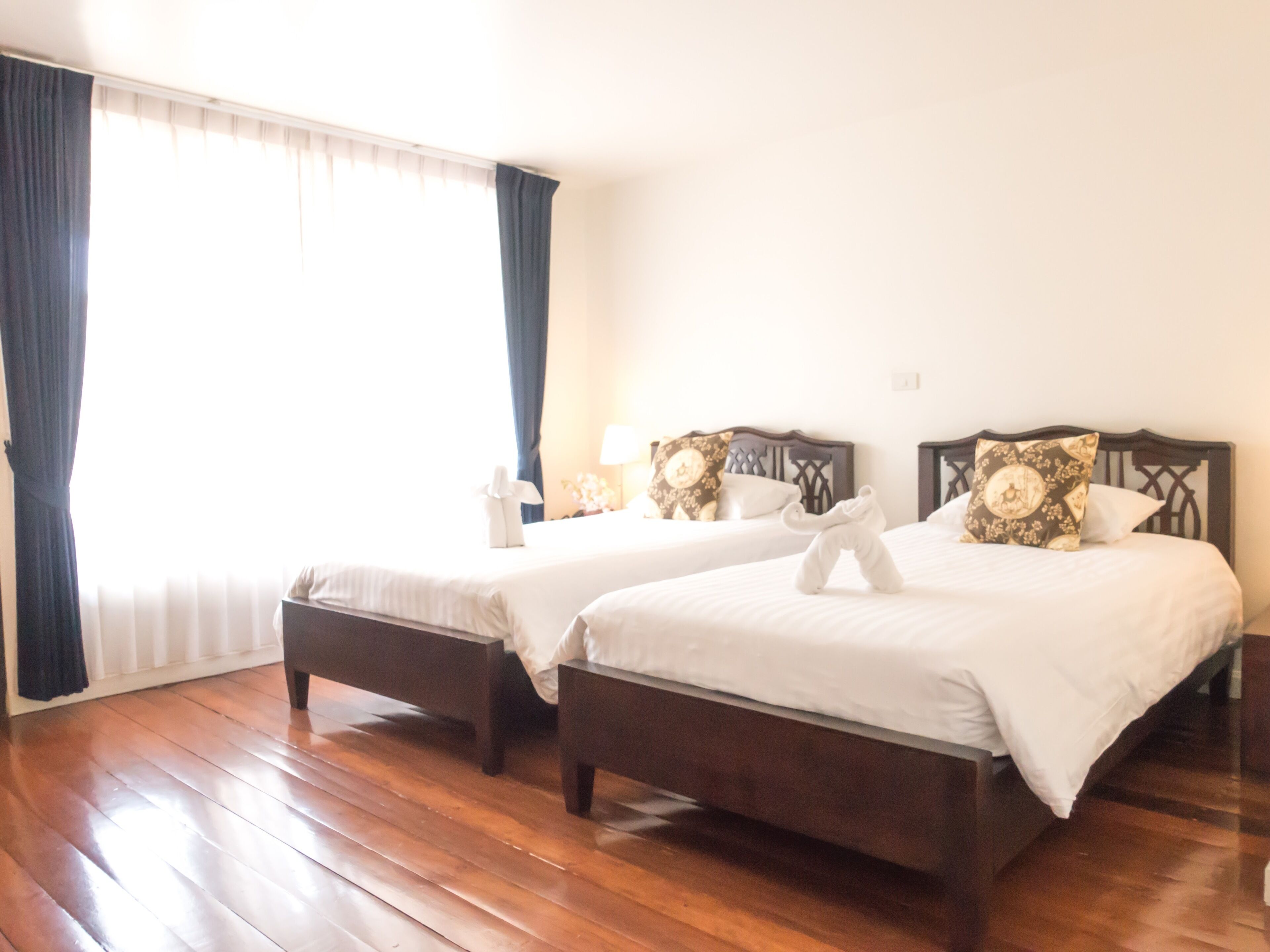 Habitación de hotel con dos camas, suelo de madera y un ventanal con cortinas.