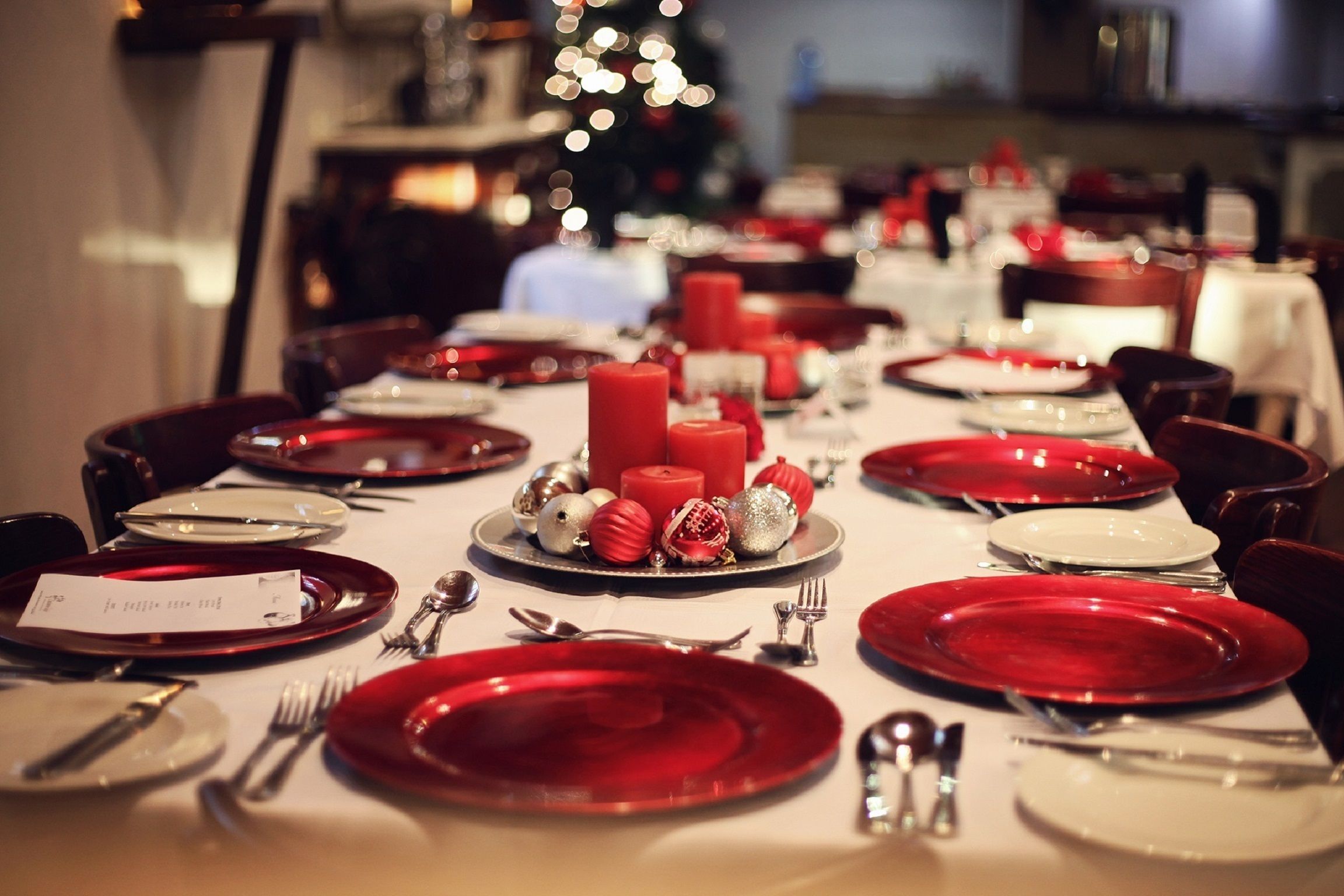 A dining table set for a meal with red and white plates, candles, and silverware.