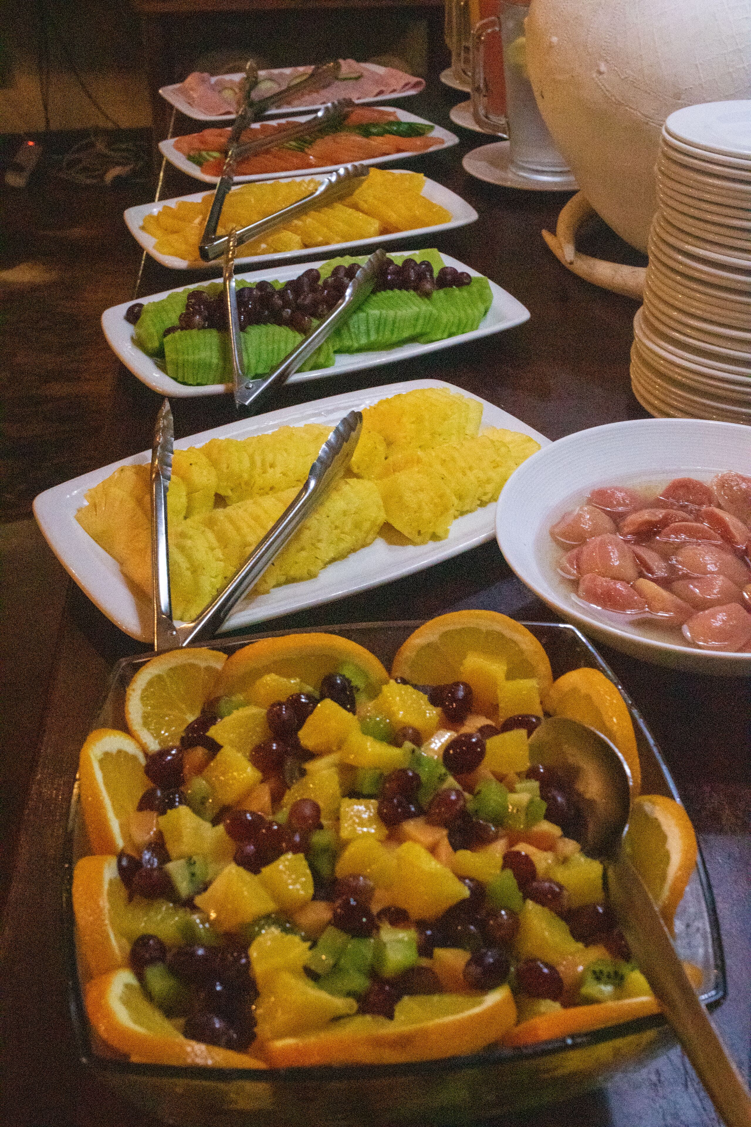 A buffet with various dishes including fruits, vegetables, and meats.