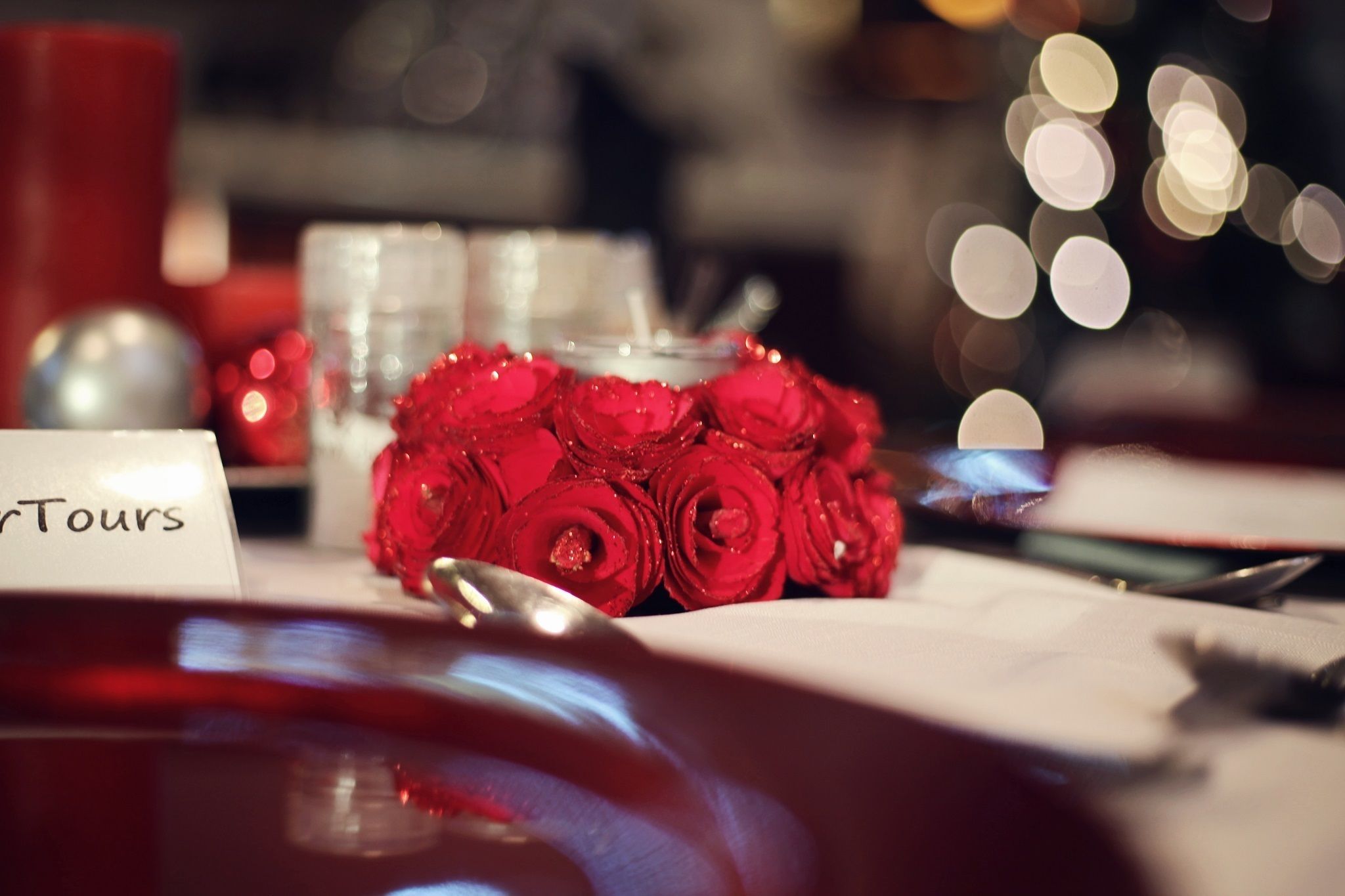 A table setting with a name card, a glass jar, and a bouquet of red roses.
