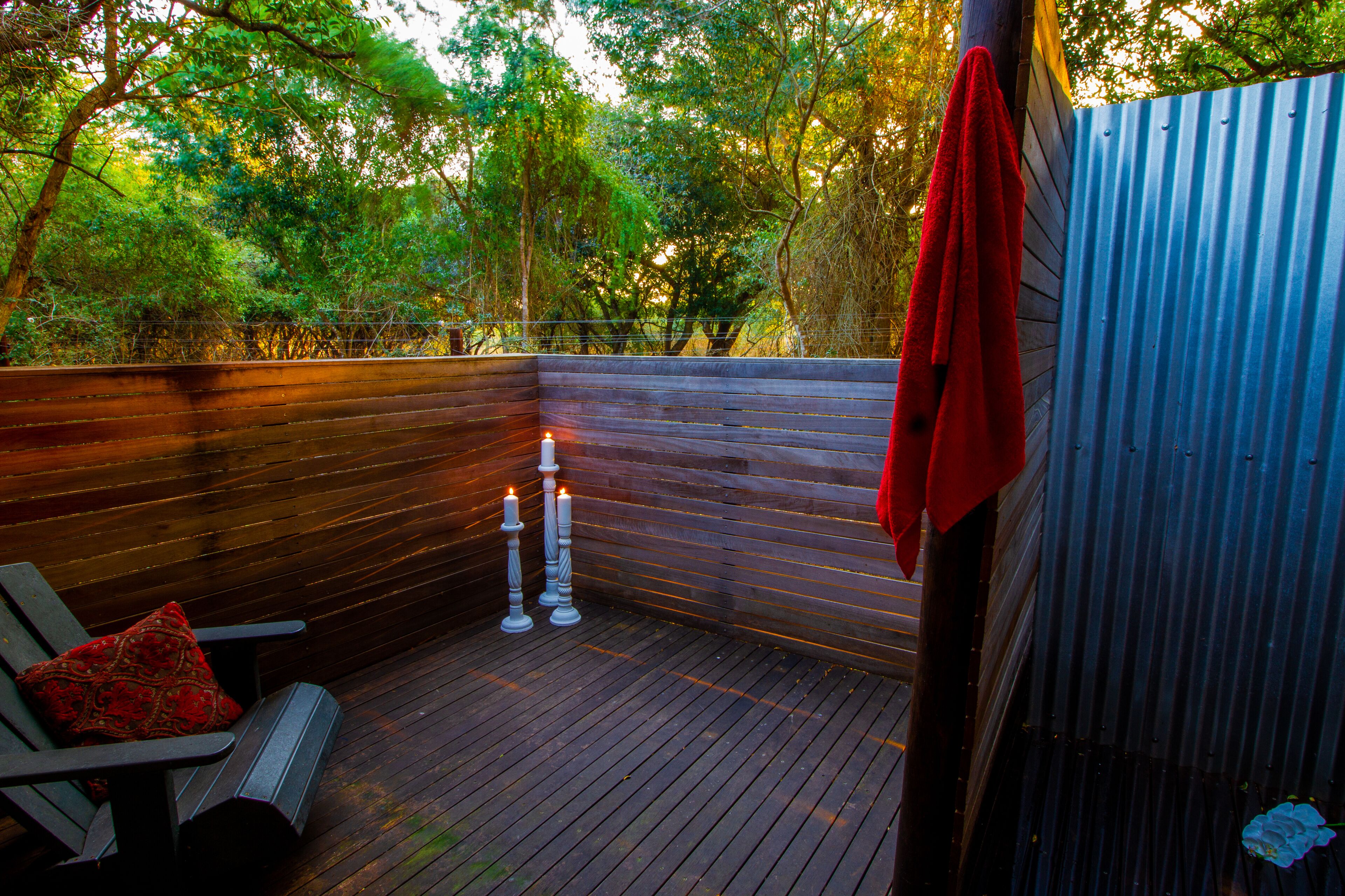 A wooden deck with a bench and candles, surrounded by trees.