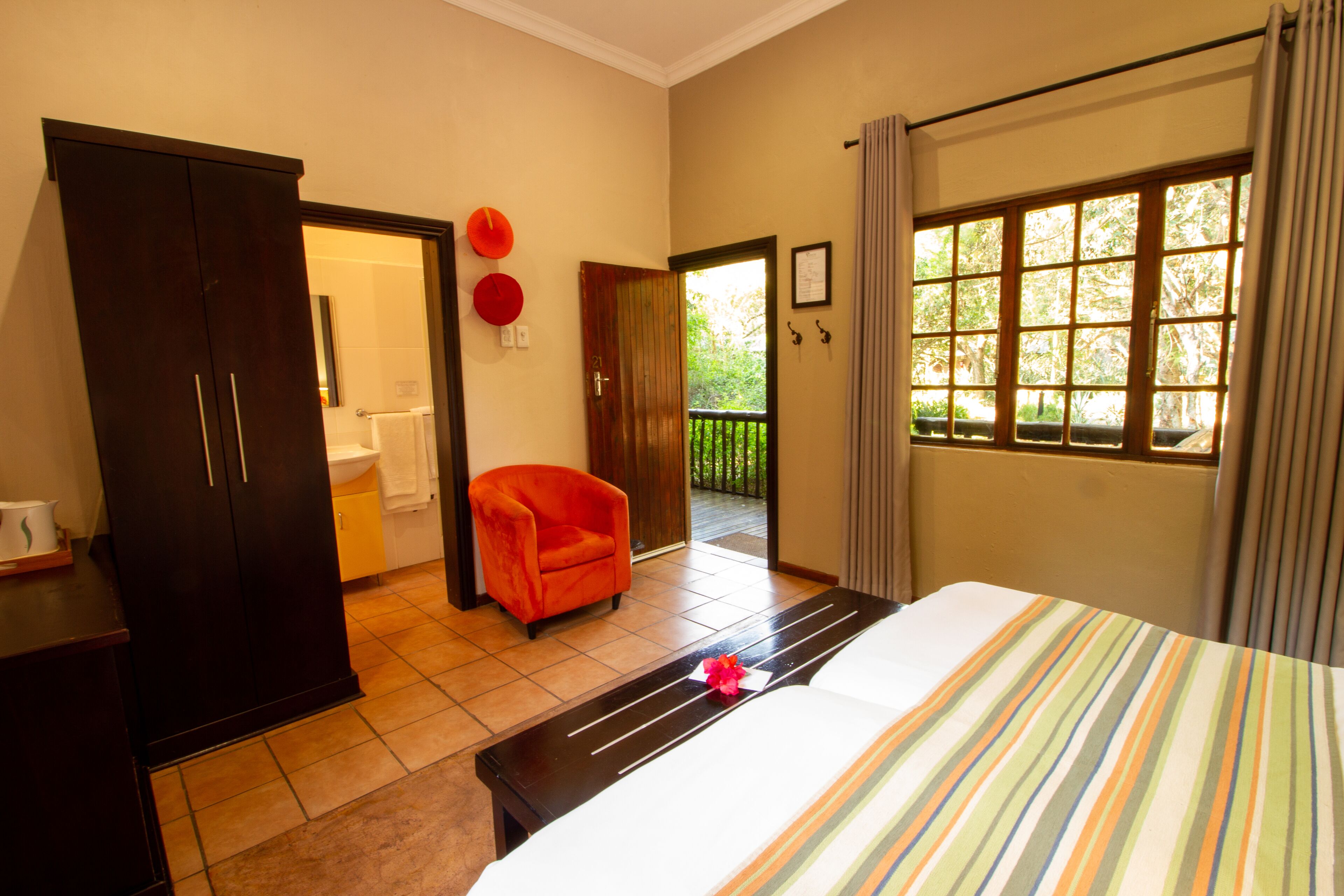 A hotel room with a bed, a wardrobe, a chair, a window with a view, and a door leading to a balcony.