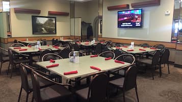 A conference room with multiple tables and chairs, a large screen displaying a presentation, and a framed picture on the wall.