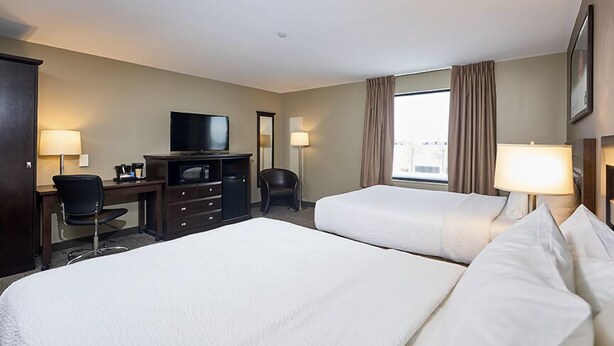 A hotel room with two beds, a desk with a chair, a television, and a window with curtains.