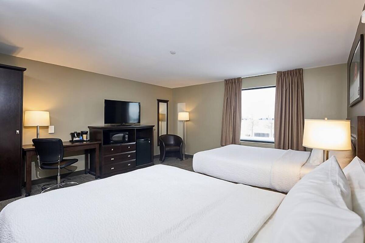 Una habitación de hotel con dos camas, un escritorio con silla, televisión y una ventana con cortinas.