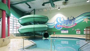 Un espace piscine intérieure doté d’un grand toboggan, d’un poste de surveillance pour les maîtres-nageurs et d’un panneau indiquant « Slushers, piscine intérieure et parc aquatique ».
