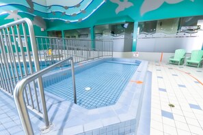 An indoor swimming pool with a tiled floor and a metal railing.