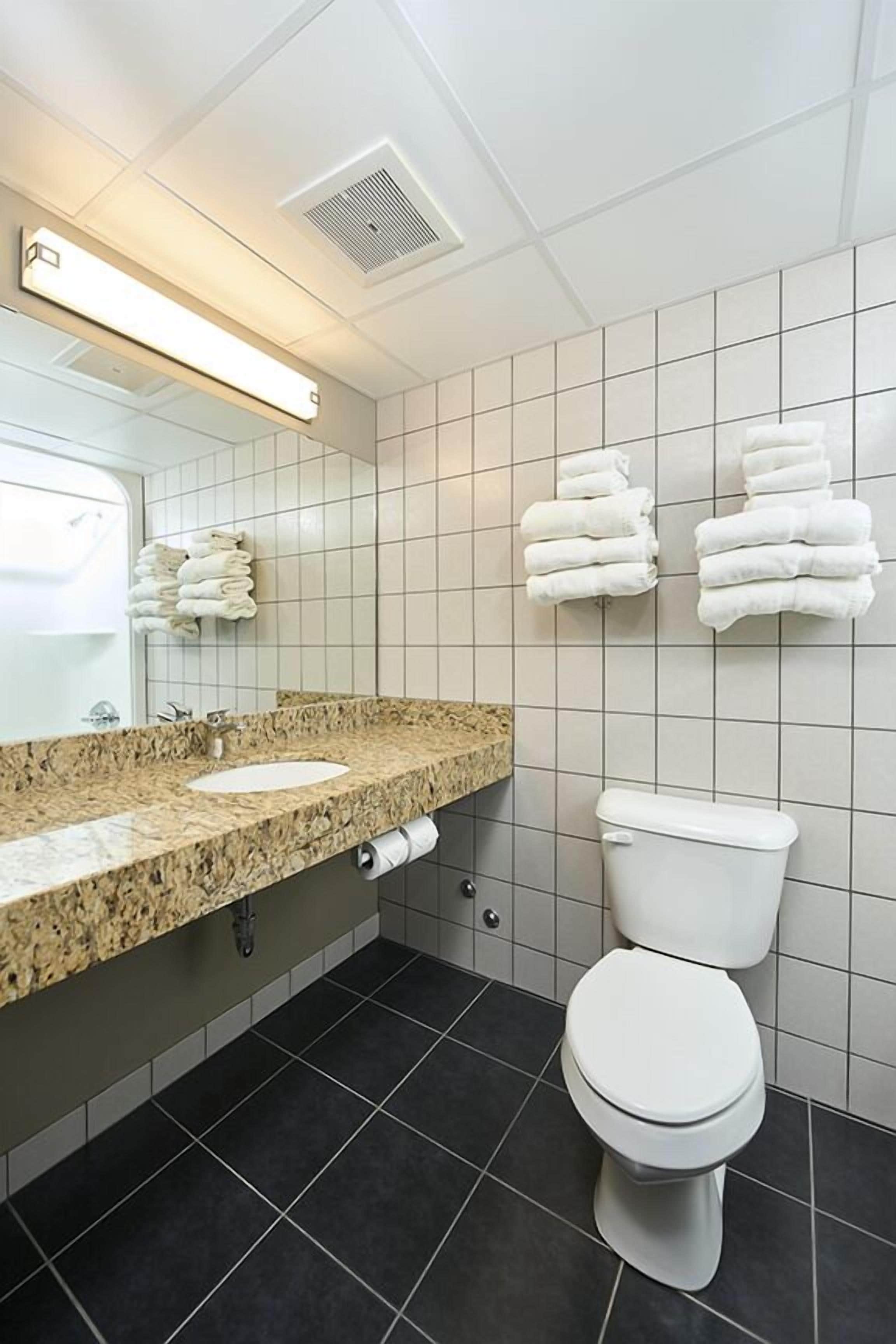 A bathroom with a granite countertop sink, a toilet, and a towel rack with folded towels.