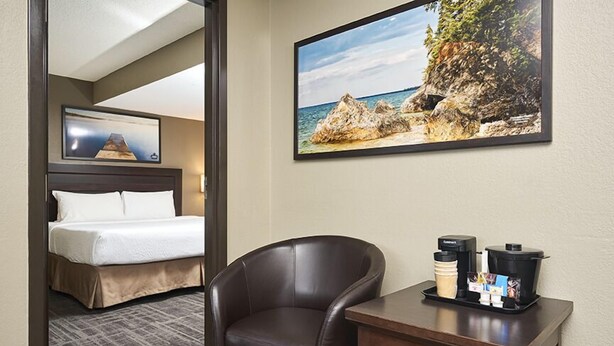 Une chambre d’hôtel équipée d’un lit, d’une chaise, d’un coin café et d’un tableau représentant un paysage côtier.