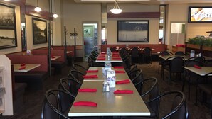 A restaurant with long tables, red napkins, and framed pictures on the walls.