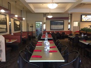 A restaurant with long tables, red napkins, and framed pictures on the walls.