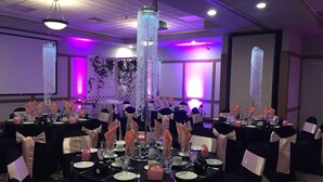 Une salle de banquet avec des tables rondes, des nappes noires et des chaises ornées de rubans roses.