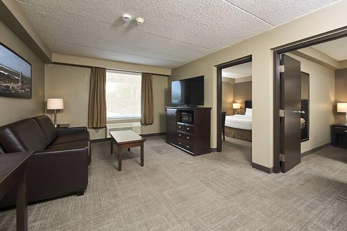 Habitación de hotel con sofá, televisión, escritorio, cama y puerta que da a otra habitación.
