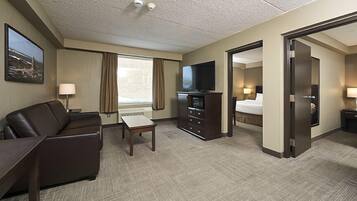 A hotel room with a sofa, a TV, a desk, a bed, and a door leading to another room.