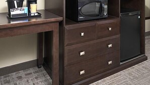 Une chambre d’hôtel dotée d’un bureau en bois foncé, d’un téléviseur à écran plat, d’un four à micro-ondes et d’un mini-réfrigérateur.