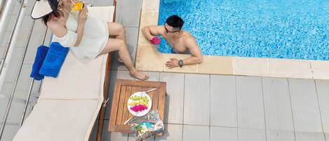 A poolside area with a table set for two, a chair, and a lounge chair.