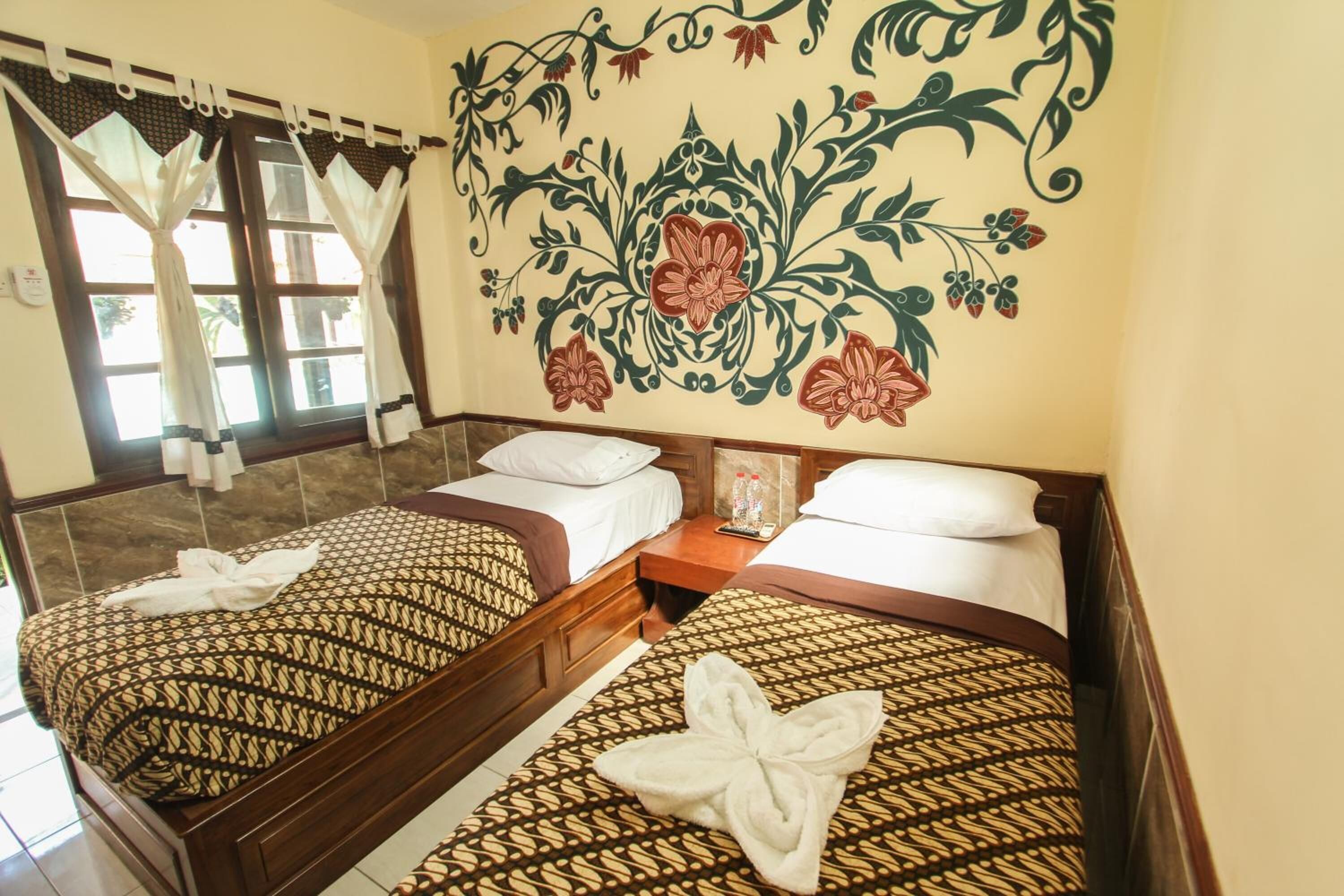 Une chambre d’hôtel avec deux lits, un décor mural floral et une fenêtre avec des rideaux.