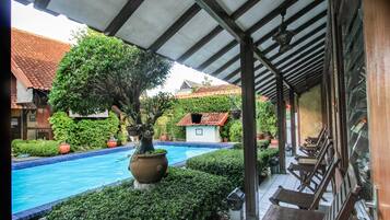 Uma área de piscina coberta, com teto em azulejos, rodeada por arbustos bem aparados e plantas em vasos.