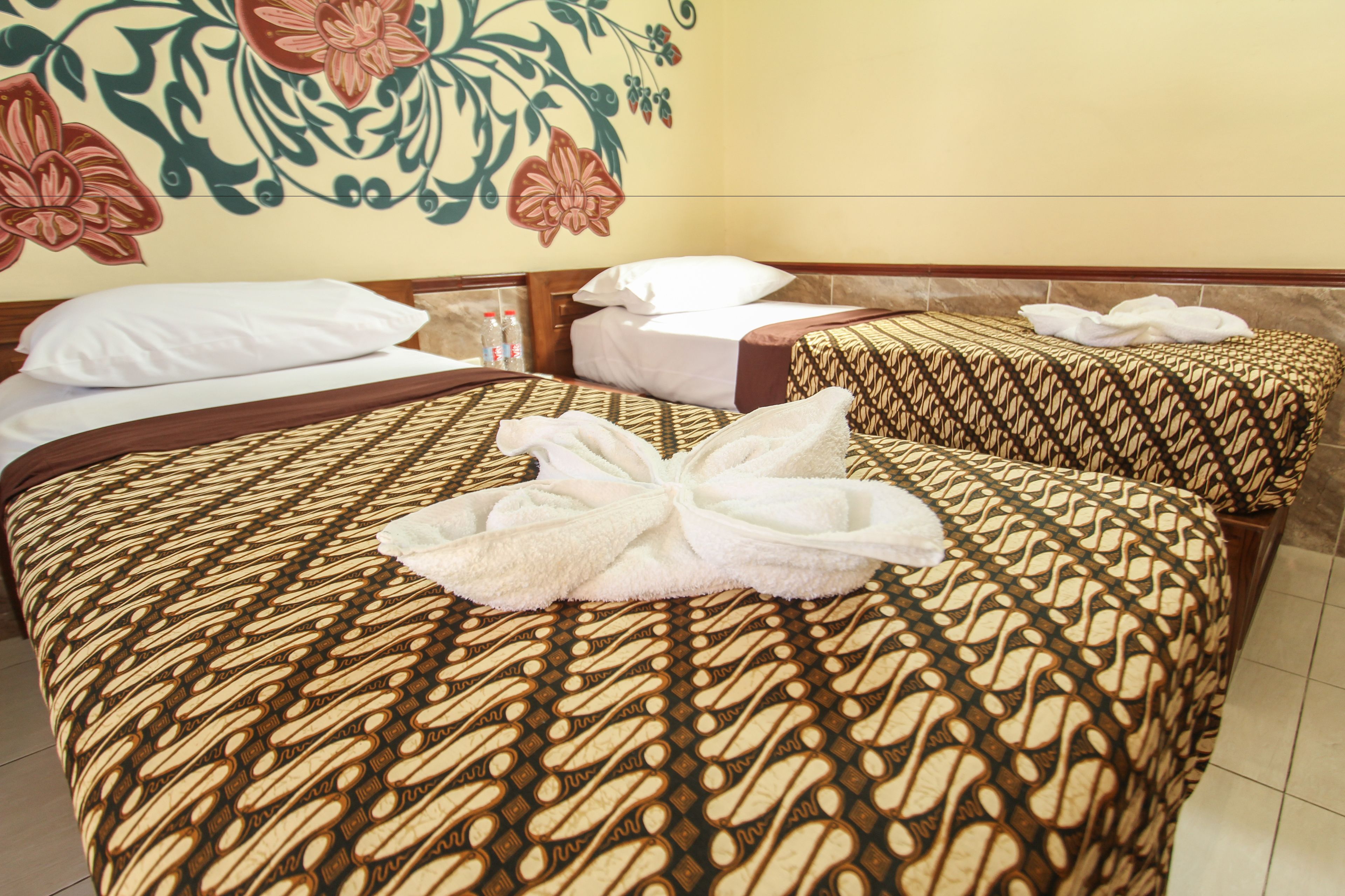 A hotel room with two beds, each with patterned bedding and a towel on one bed.