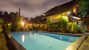 Une piscine entourée de bâtiments traditionnels aux toits de tuiles et agrémentée de plantes en pot.