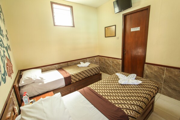 A hotel room with two beds, a wooden door, a small window, and a flat-screen TV mounted on the wall.