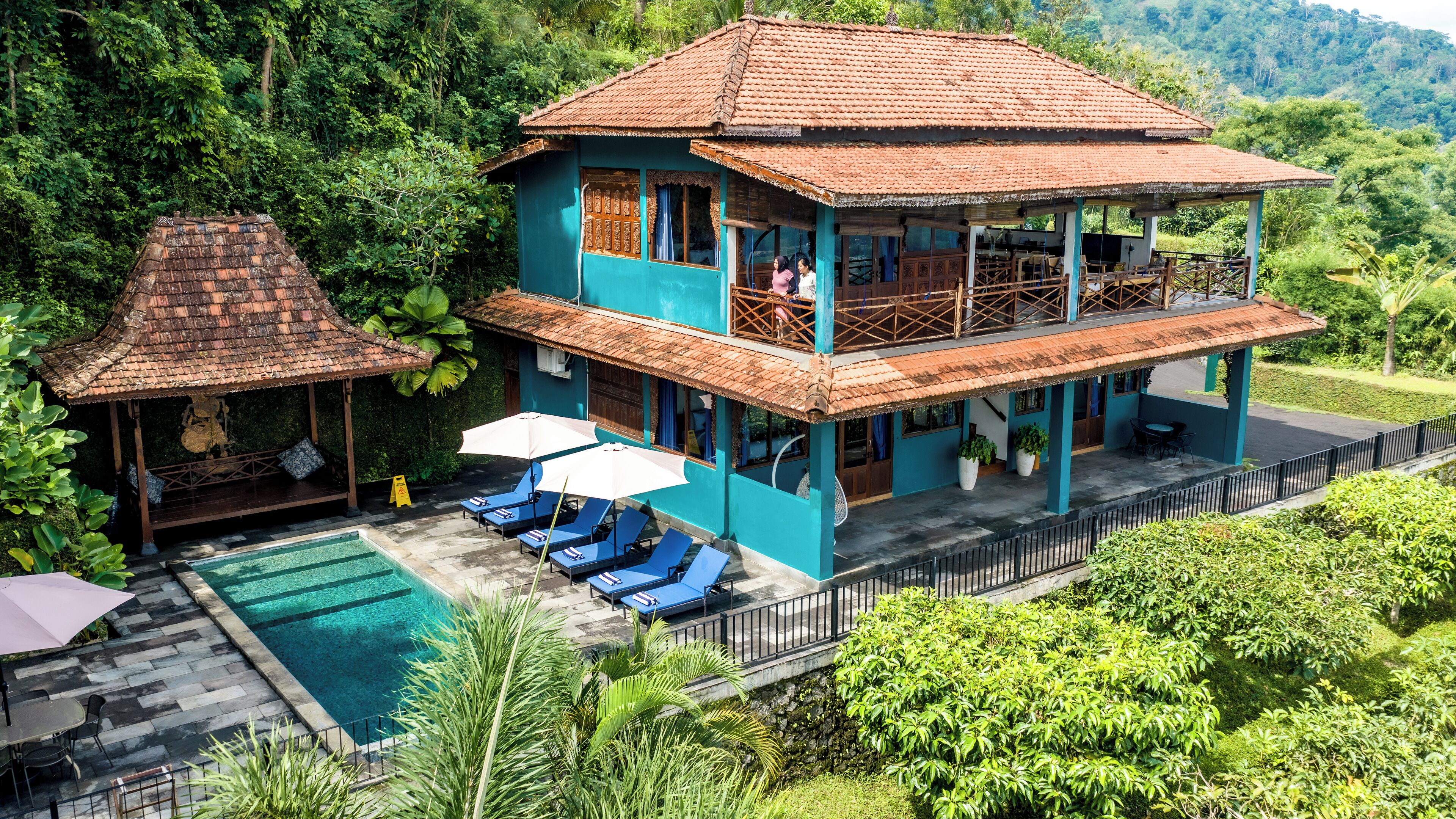 Uma casa de dois andares com piscina, varanda coberta e vegetação exuberante.