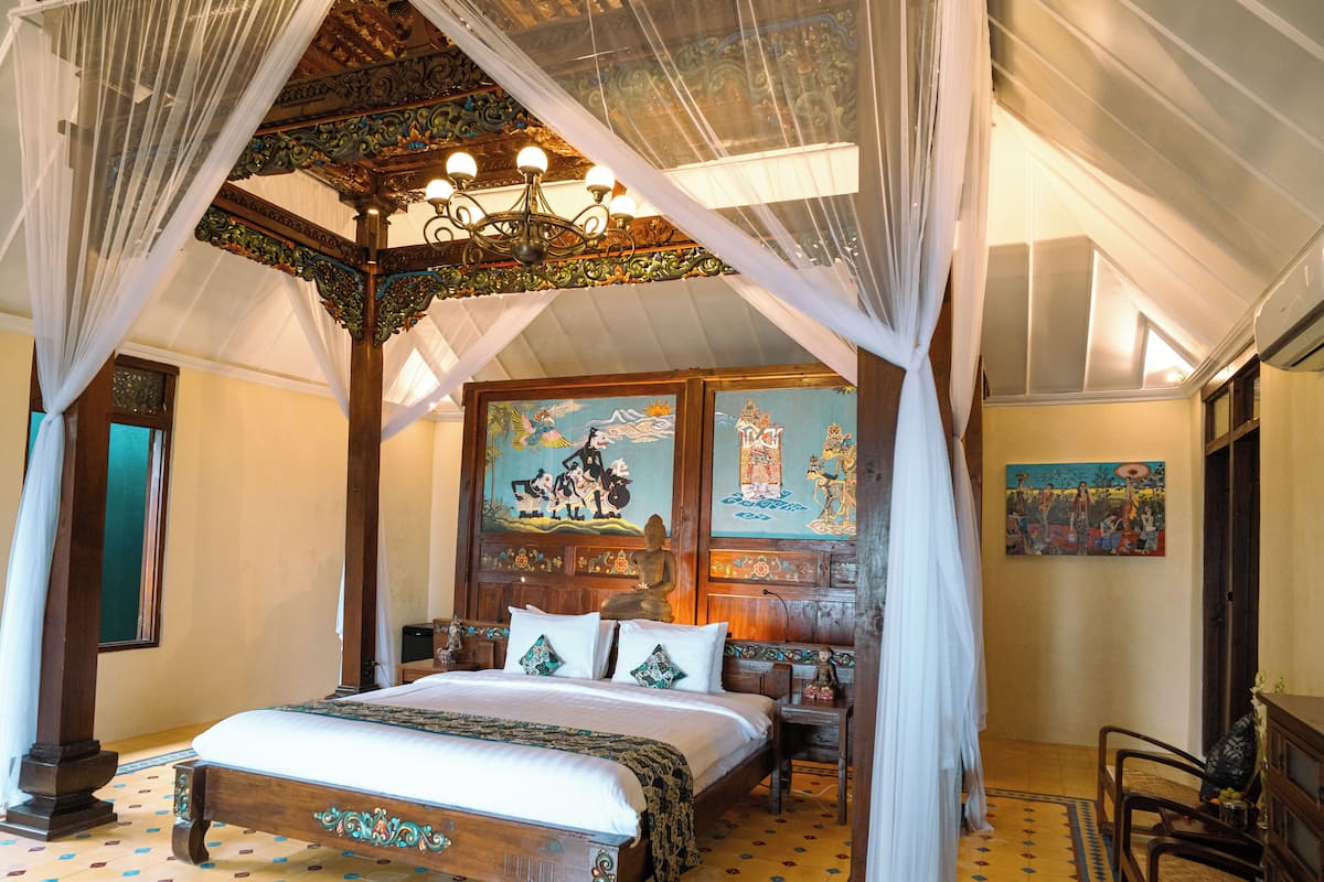 A traditional room with a four-poster bed, a chandelier, and a mural on the wall.
