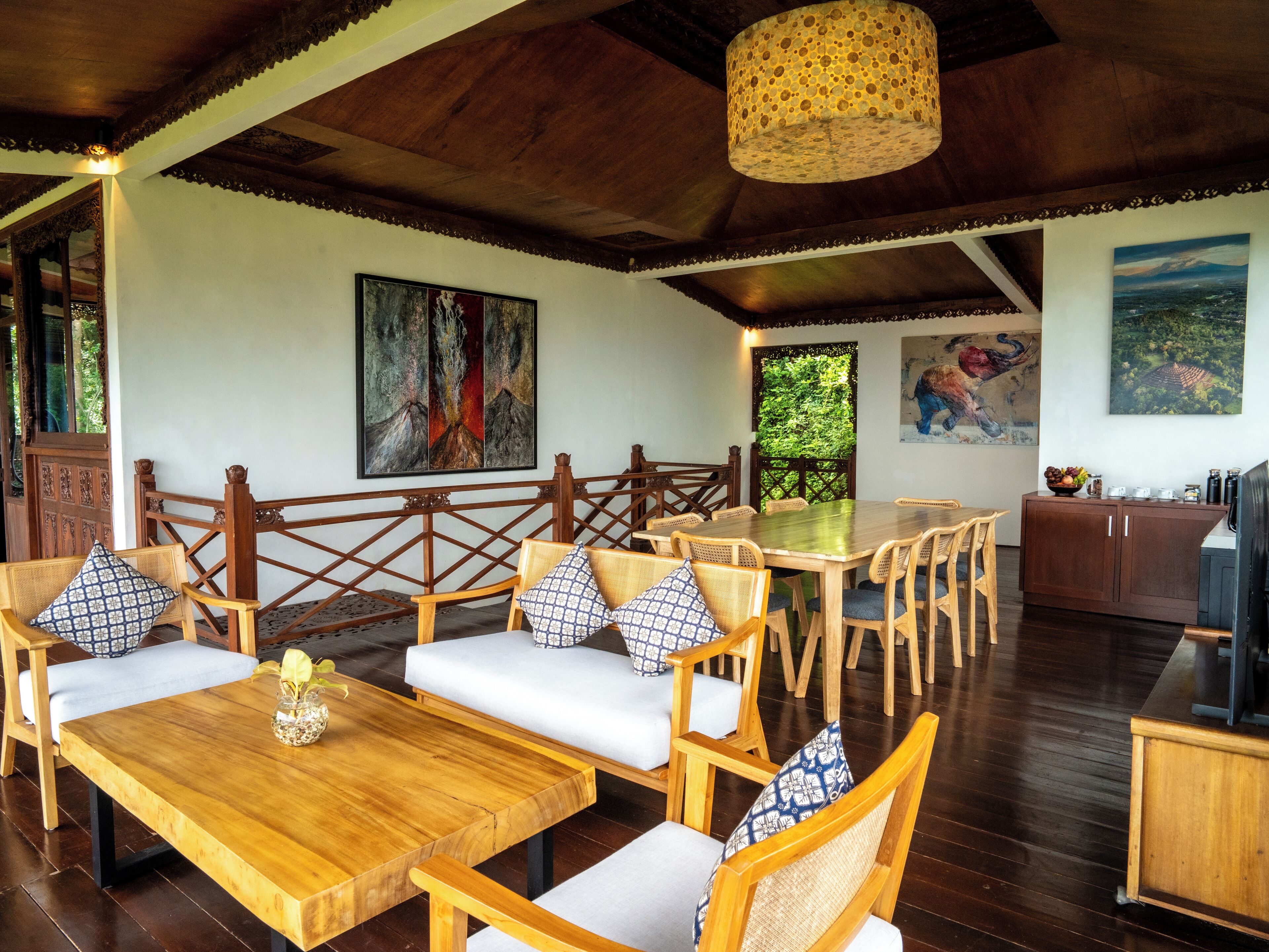 A dining area with wooden furniture, a large painting, and a view of greenery.