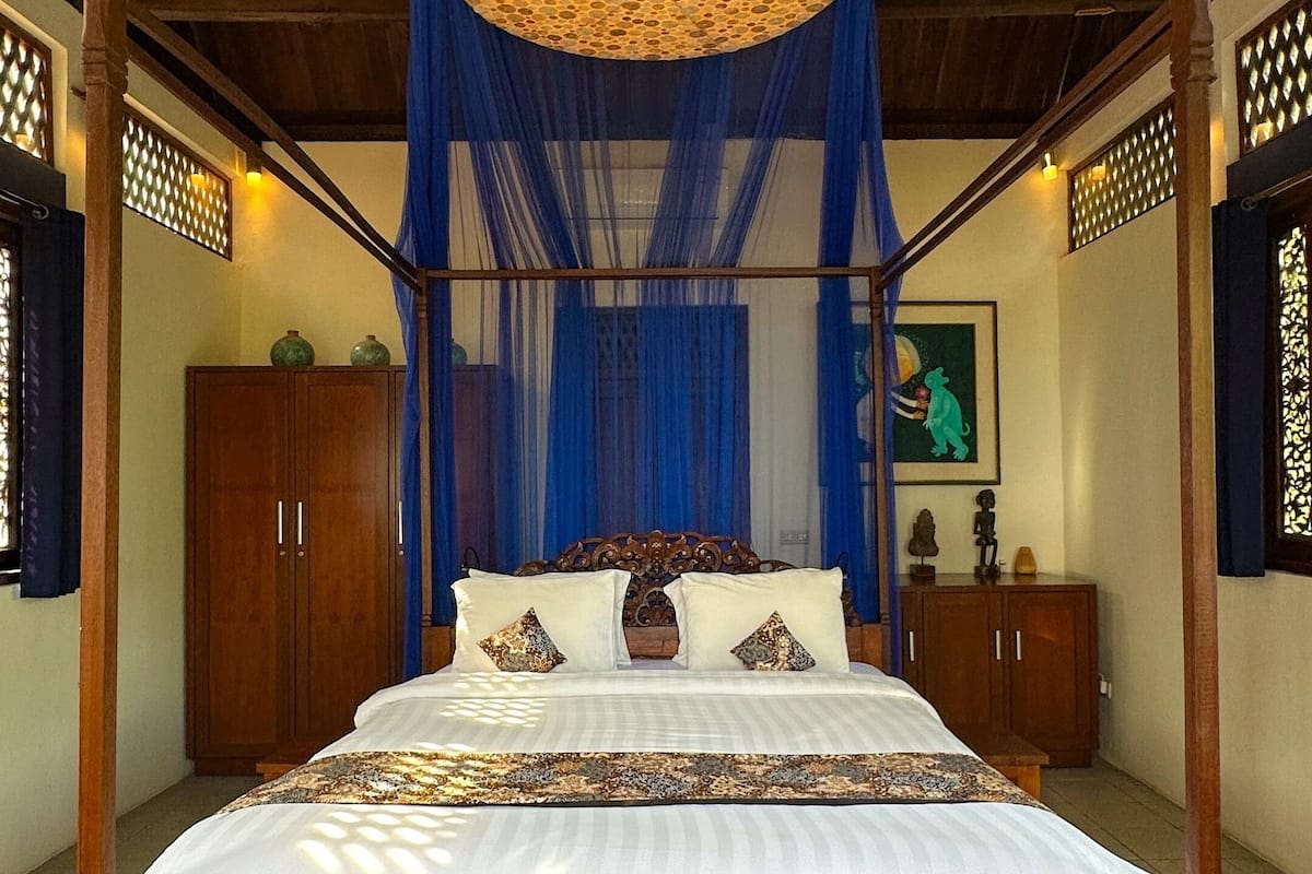 A four-poster bed with a canopy, wooden headboard, and a decorative ceiling light.