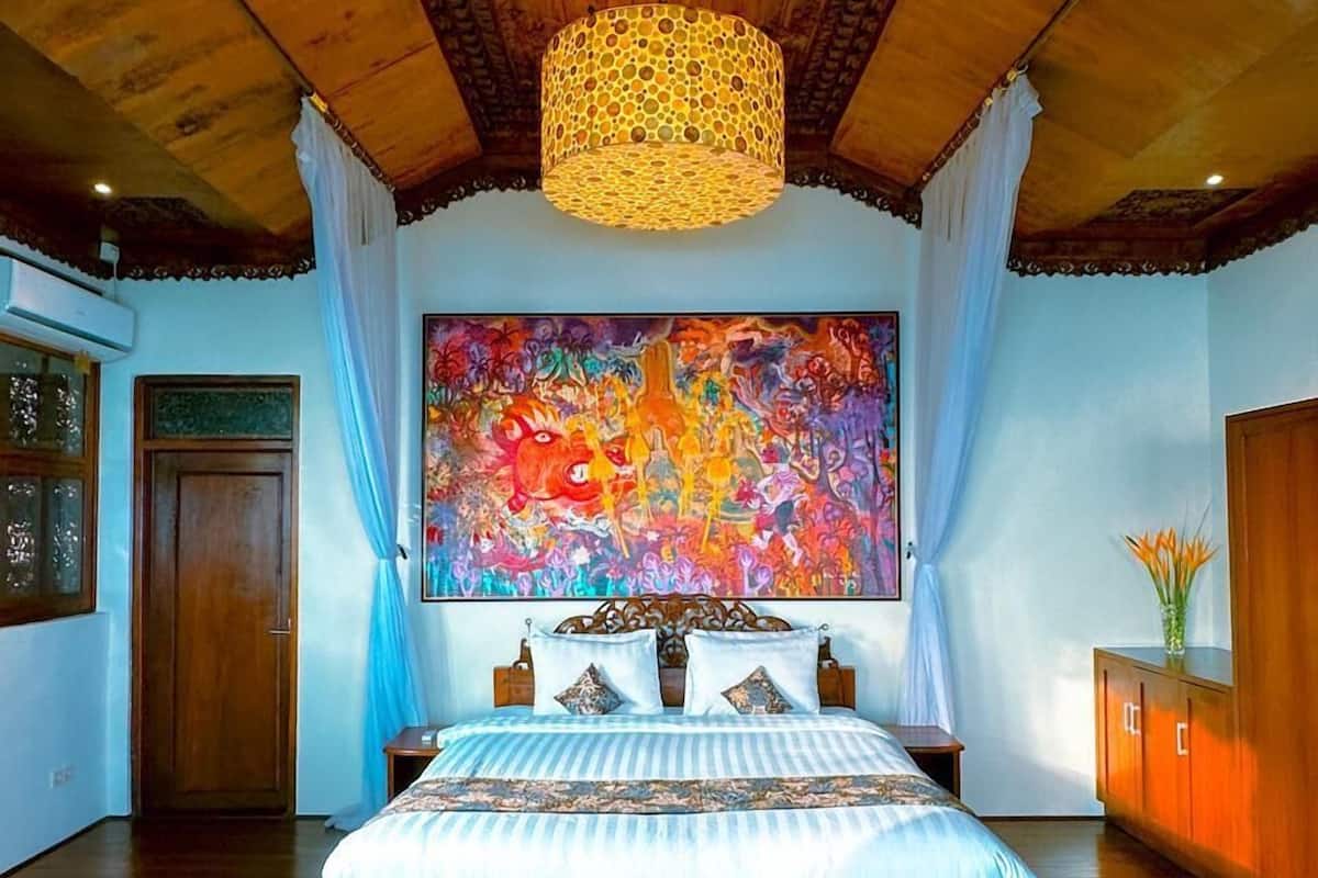 A spacious bedroom with a large bed, a wooden ceiling, and a vibrant abstract painting on the wall.