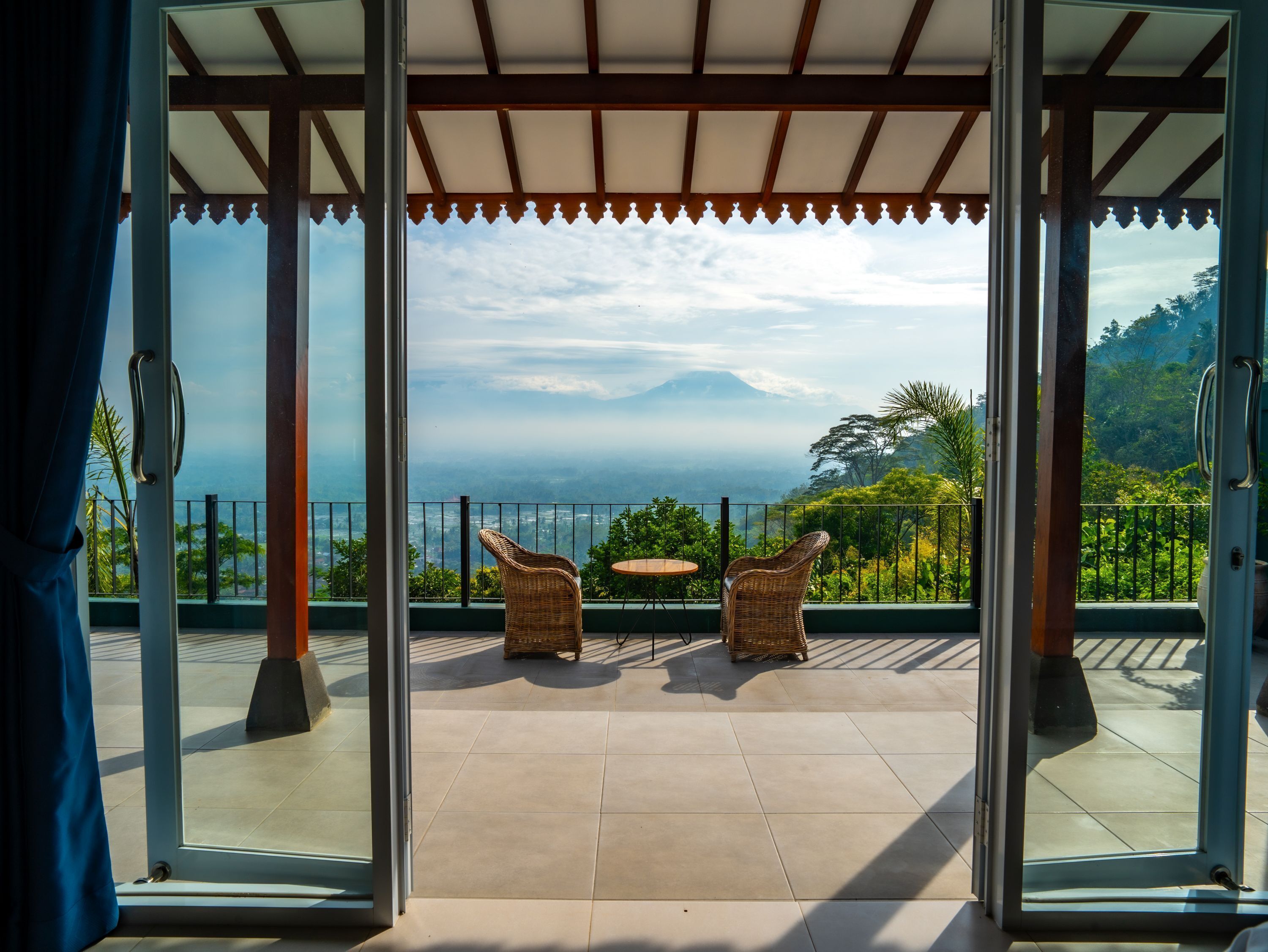 A balcony with two wicker chairs and a small table, overlooking a mountainous landscape.
