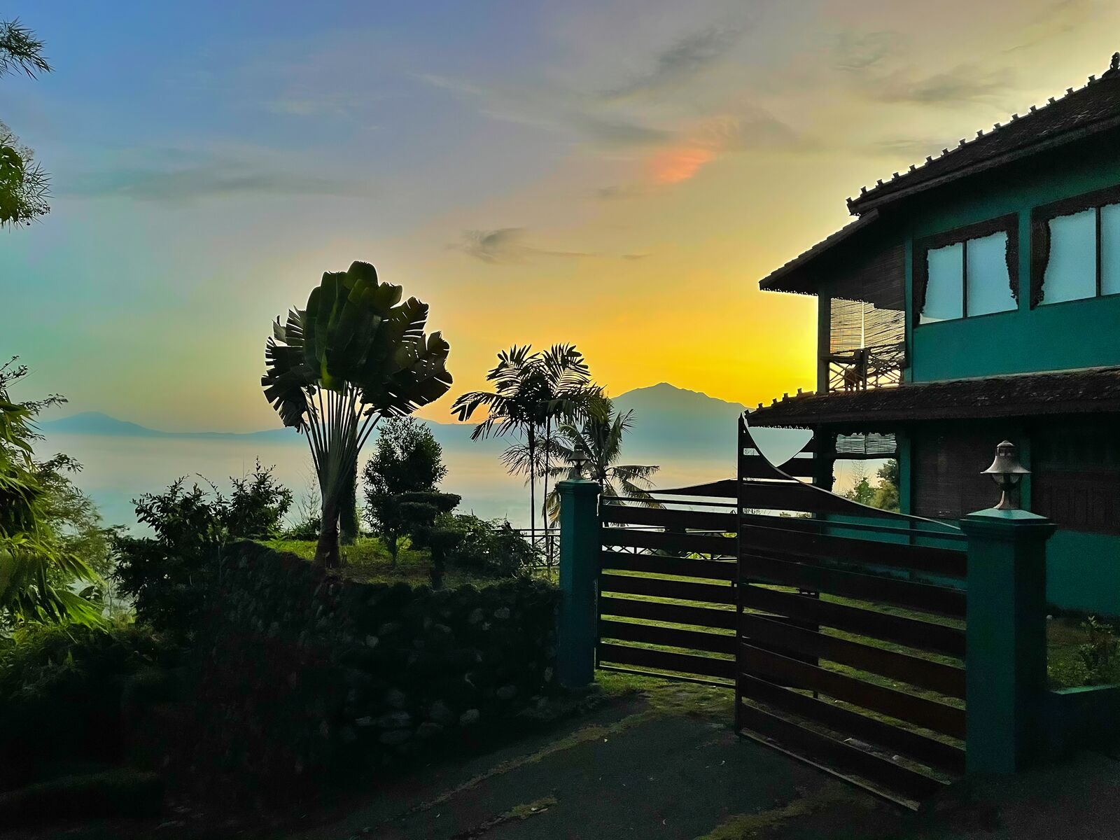 Uma casa com um portão verde e uma montanha ao fundo.