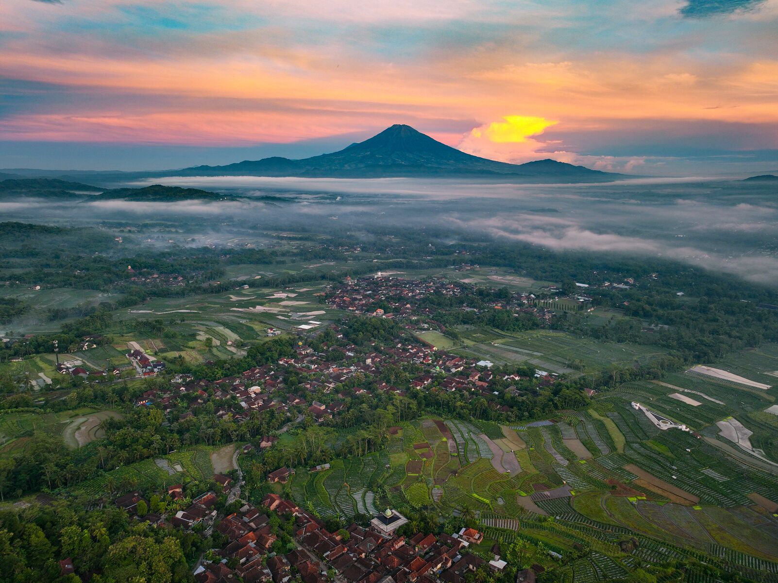An aerial view of a town with terraced fields and a mountain in the background.