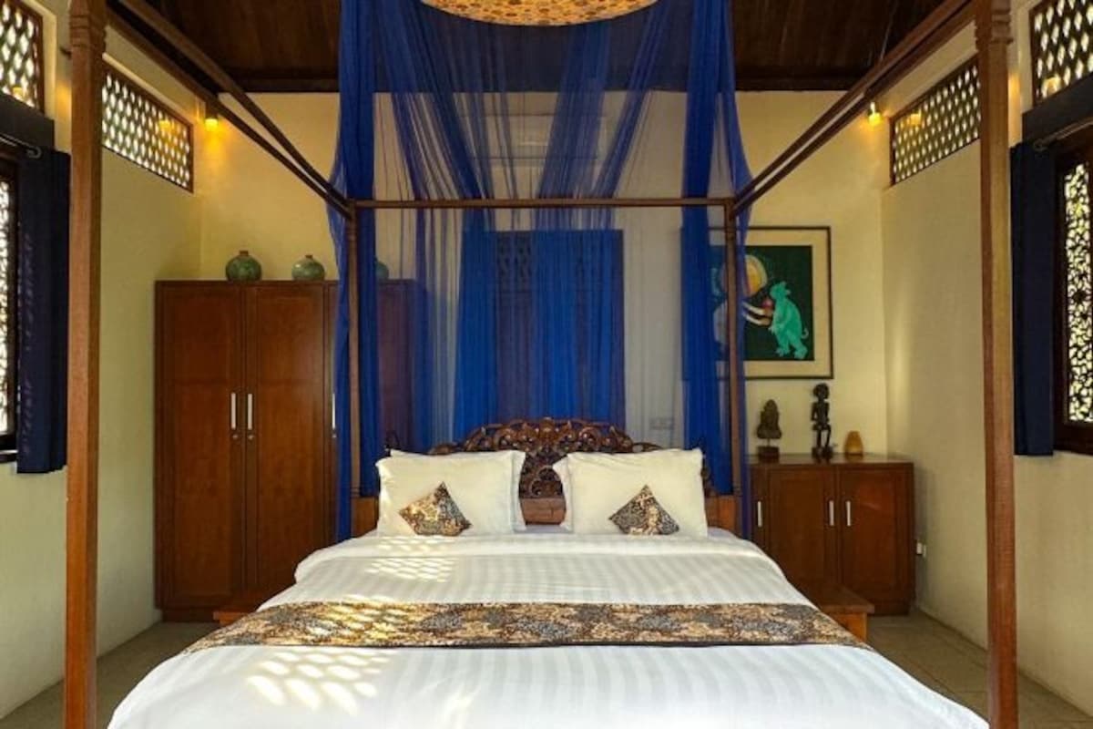 A four-poster bed with a canopy, wooden furniture, and artwork on the walls.