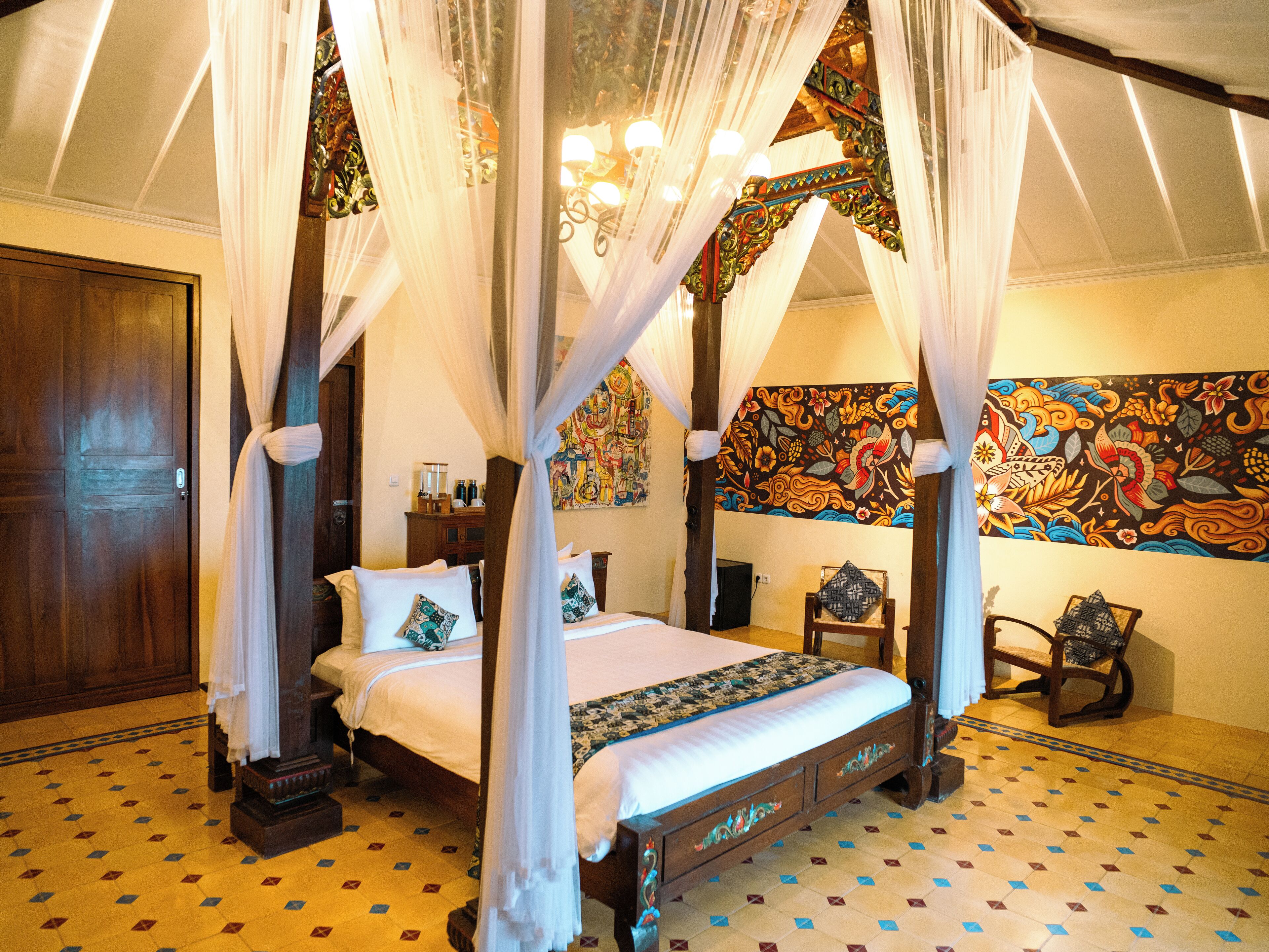 A four-poster canopy bed with a floral-patterned bedspread, a wooden nightstand, and a chair with a woven seat.