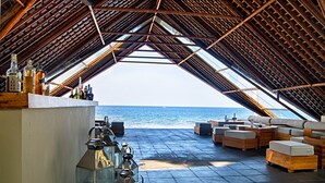 Un bar al aire libre con vista al mar, que presenta techo de madera y zona de estar.