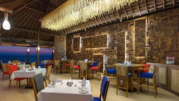 A restaurant with wooden walls, tables set with white tablecloths, and chairs with red and blue cushions.