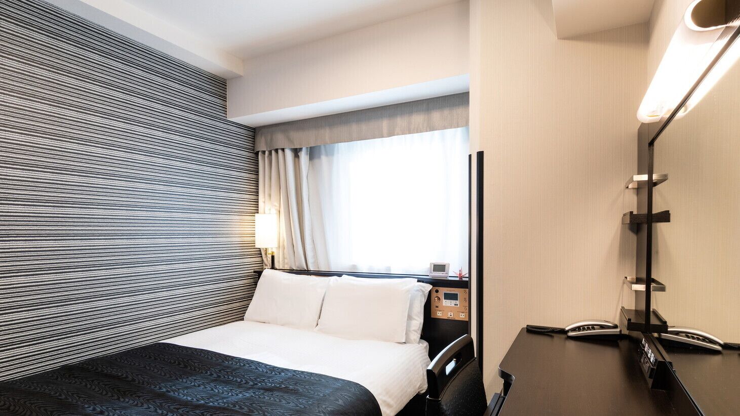 Habitación de hotel con cama, mesita de noche, lámpara y ventana con cortinas.