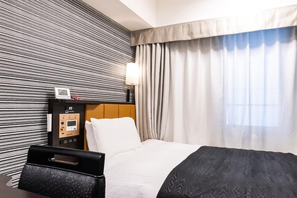 A hotel room with a bed, a control panel, a TV, and a window with curtains.