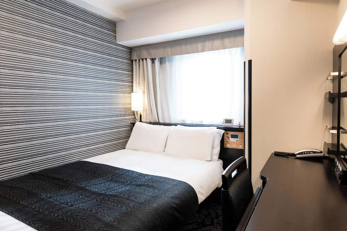 A hotel room with a bed, bedside table, lamp, and a mirror.