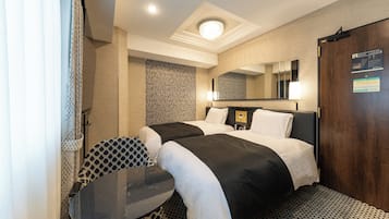 A hotel room with two beds, a small table, a chair, a mirror, and a door with an emergency exit sign.