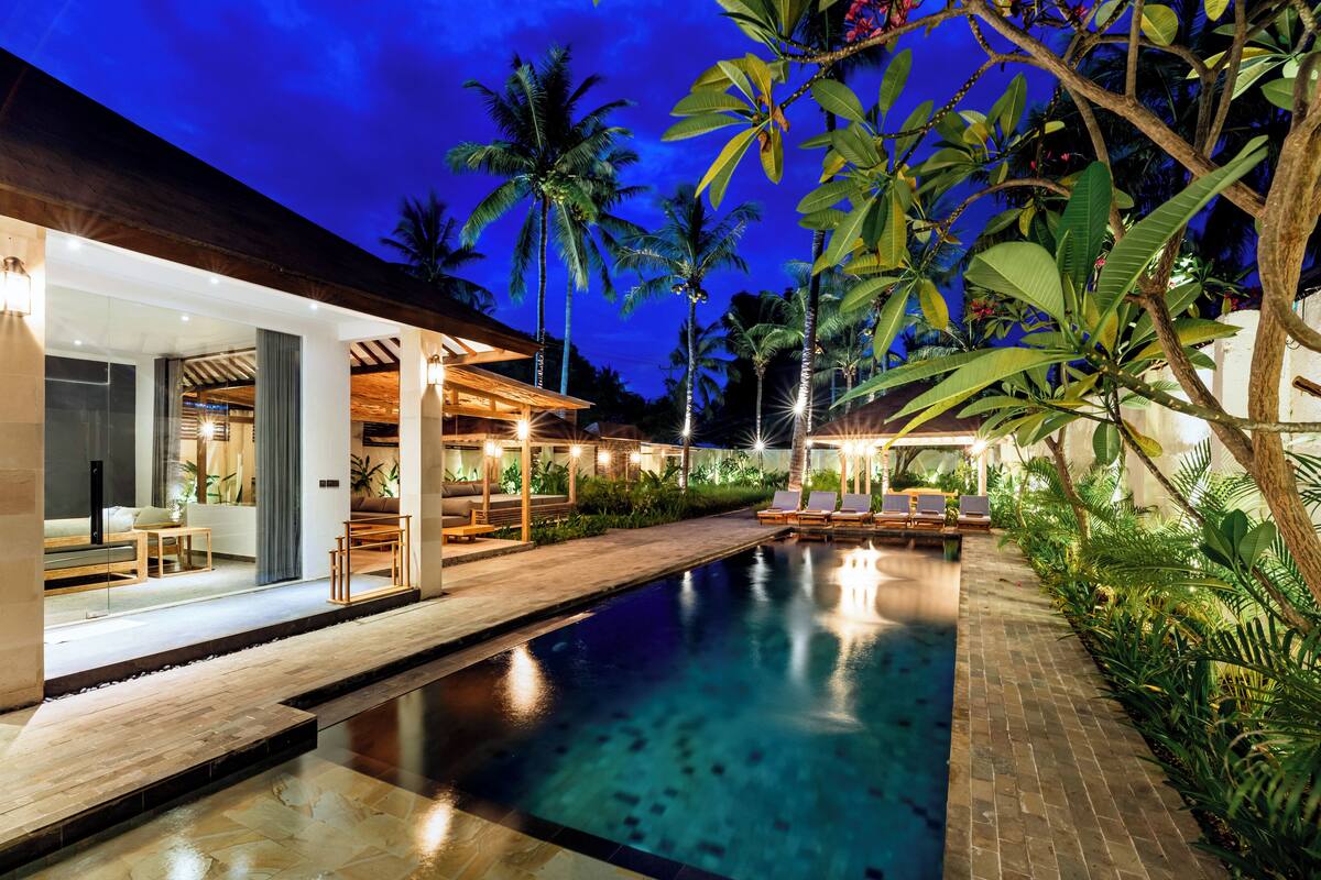 A pool area with lounge chairs, a wooden deck, and tropical plants.